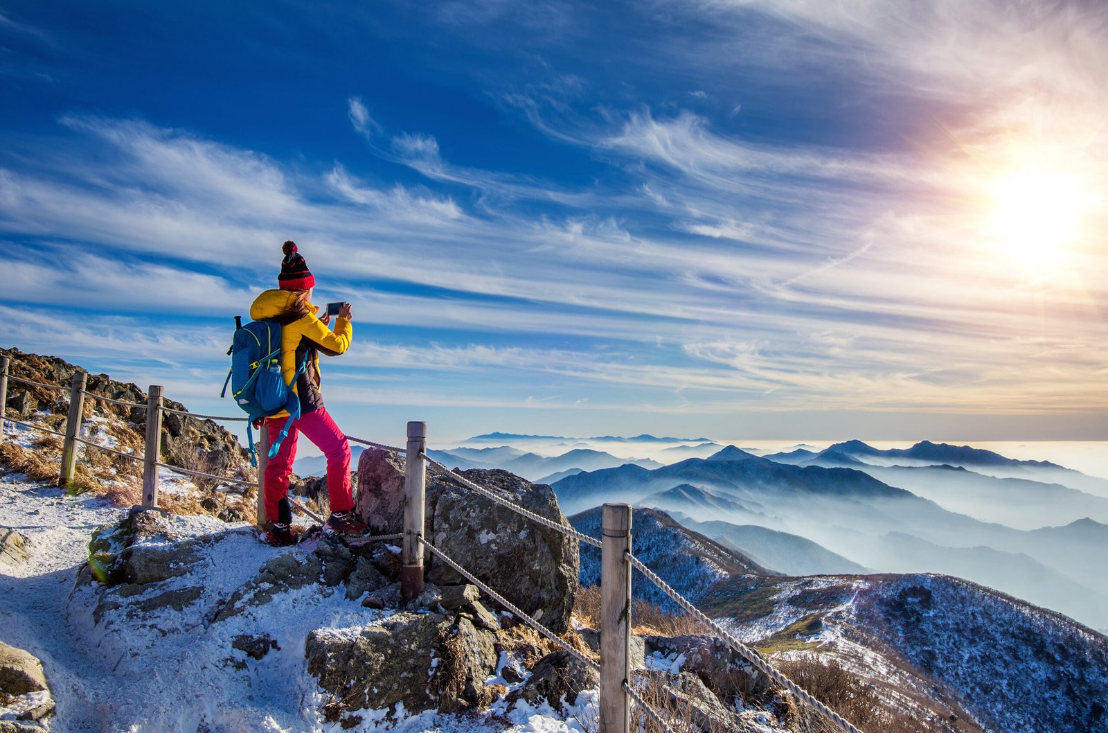 Young woman hiker taking photo with smartphone on mountains peak in winter.